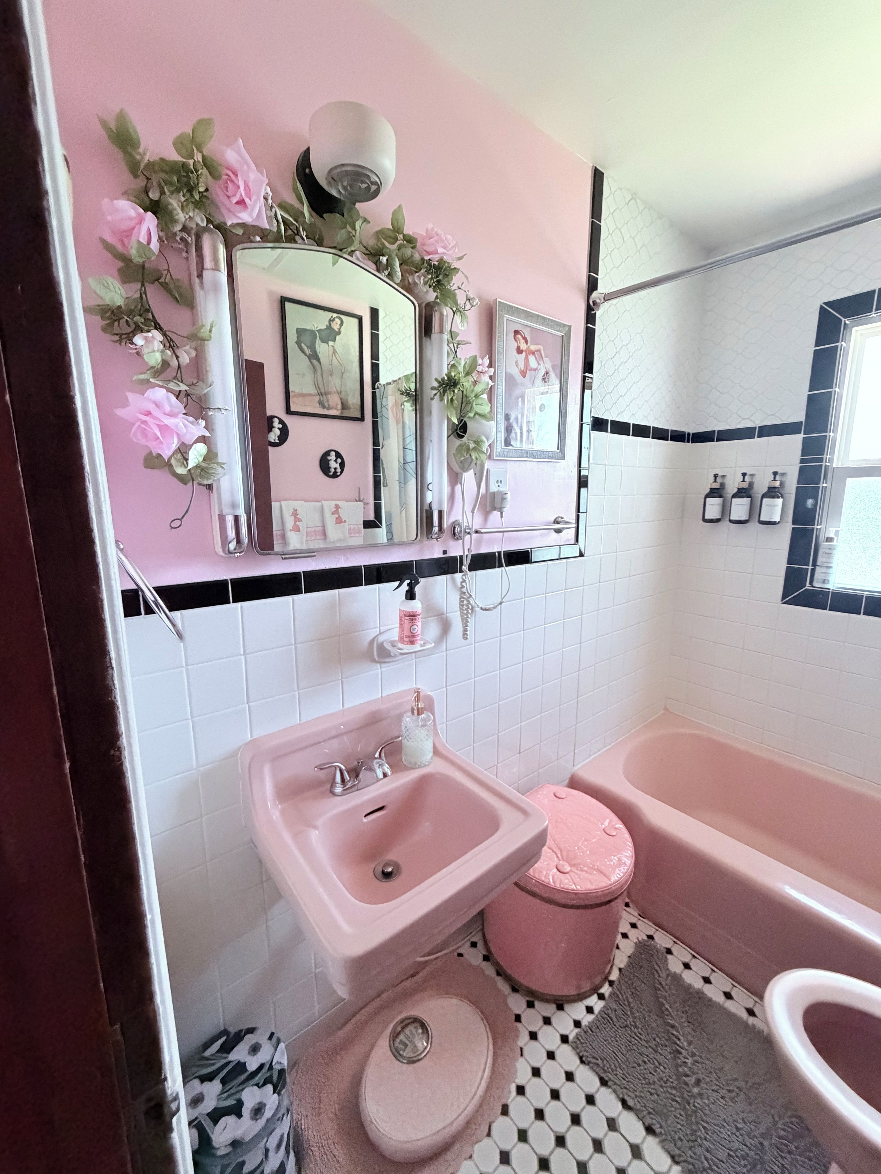 A bathroom with a pink sink, a bathtub, and a toilet. There are decorative plants and a mirror above the sink.