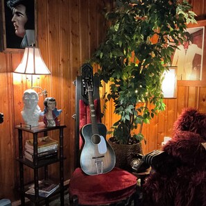 A room with wooden paneling, a guitar, a lamp, a bust sculpture, and a potted plant.