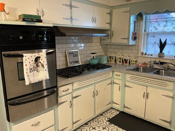 A kitchen with a stainless steel refrigerator, a gas stove, and white cabinets with metal handles.