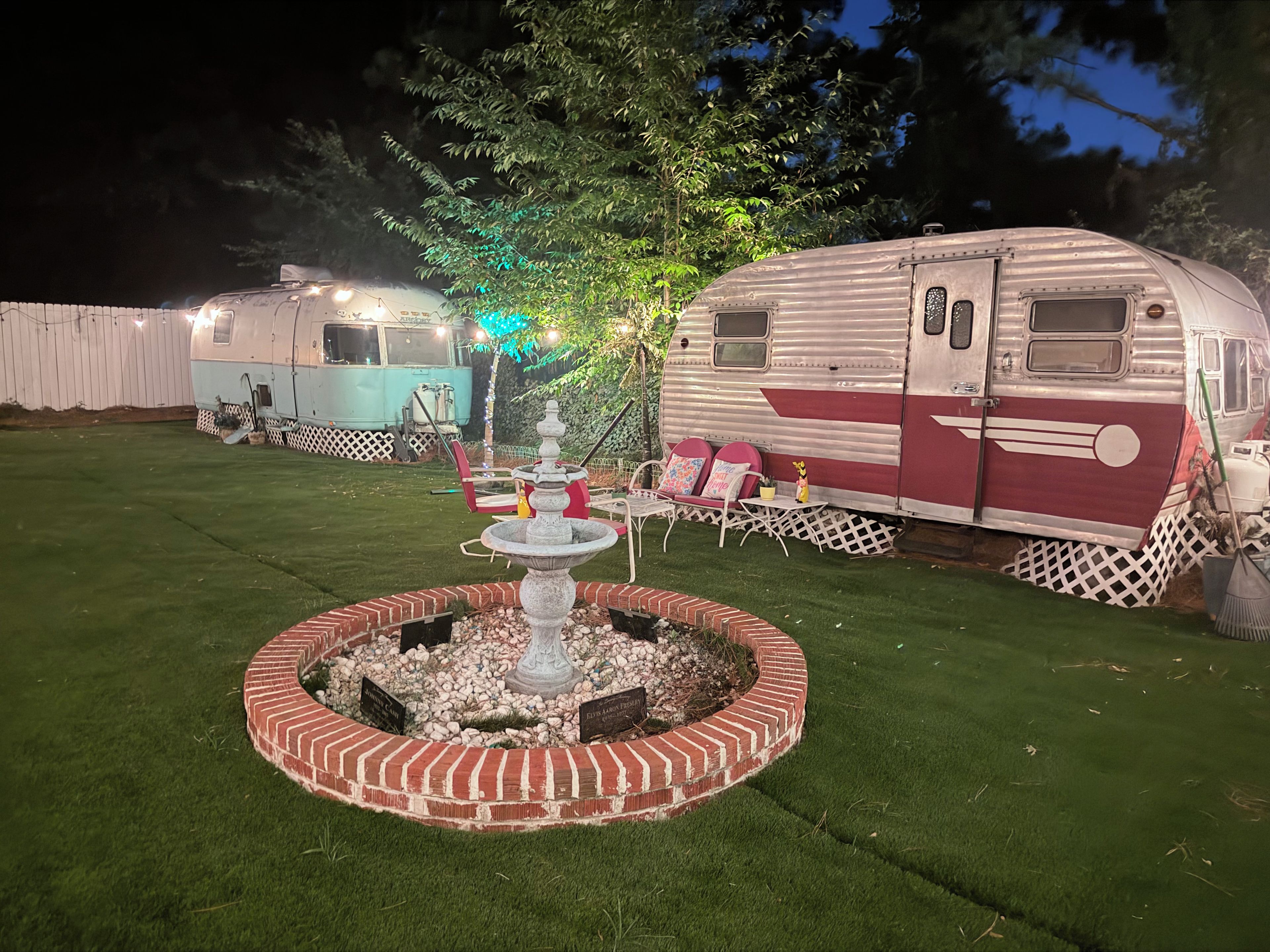 Een verzorgd gazon met een decoratieve fontein en een zitgedeelte, omringd door campers.