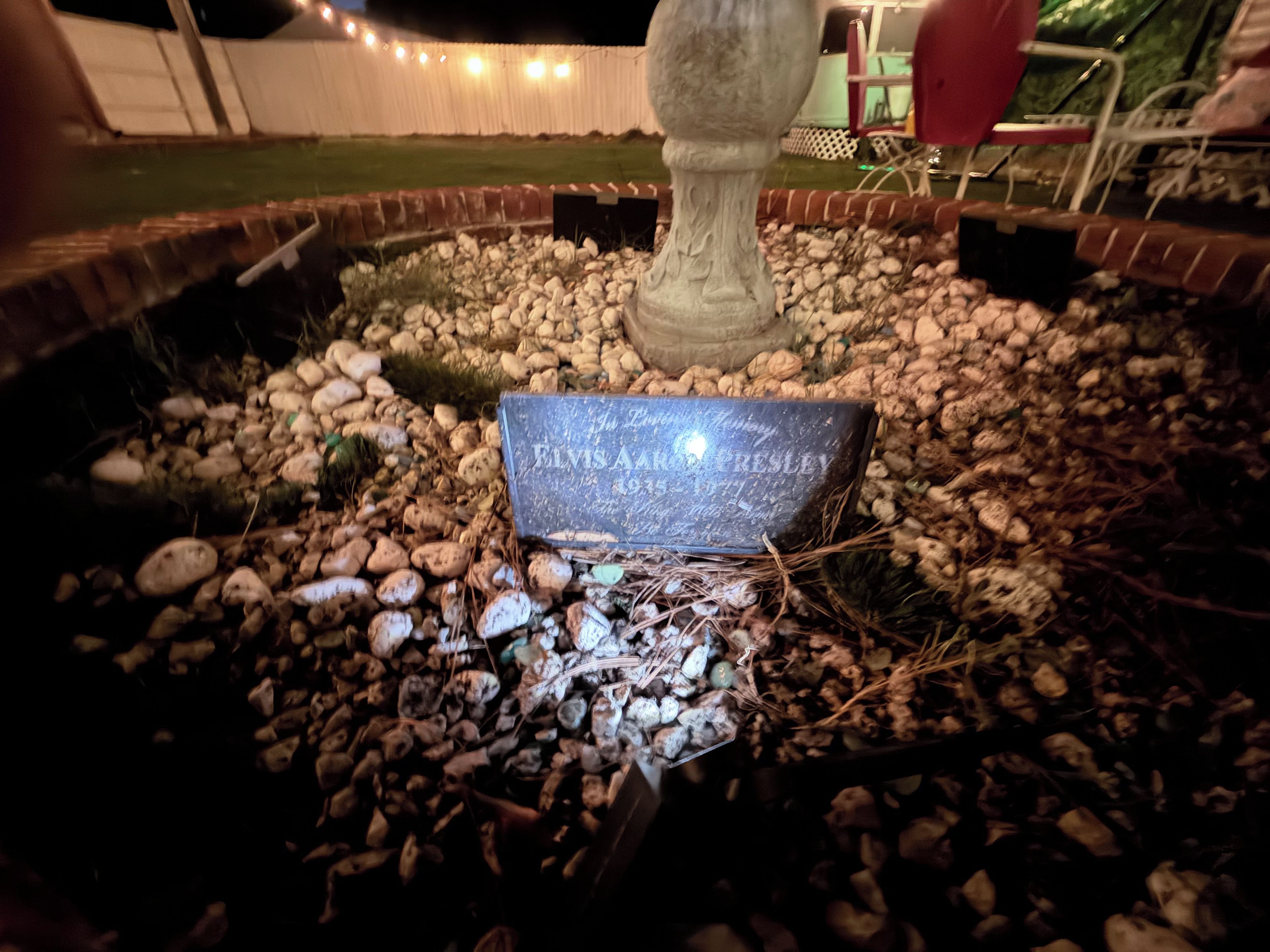 A stone monument with engraved text, surrounded by a gravel bed and small plants.