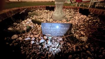 A stone monument with engraved text, surrounded by a gravel bed and small plants.