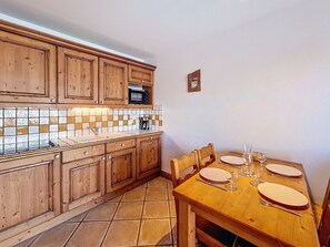 A kitchen with wooden cabinets, a tiled backsplash, a microwave, and a dining table set for four. - Bright apartment near slopes - 4 guests (Les Menuires)