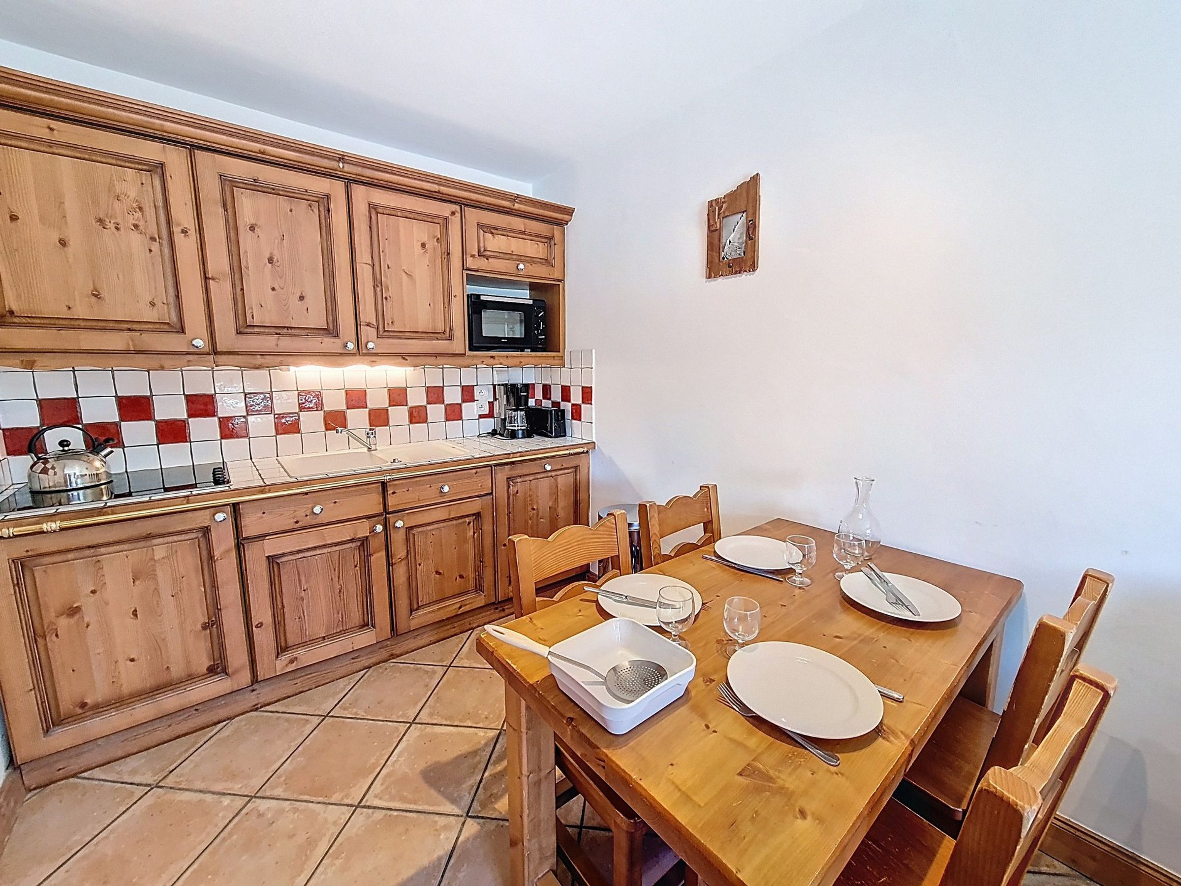 A kitchen with wooden cabinets, a tiled backsplash, a microwave, and a dining table set with plates, glasses, and cutlery.