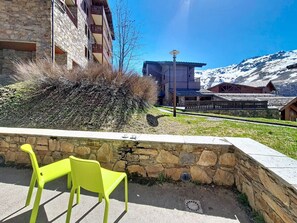 A stone building with a balcony, a chair, and a view of snow-capped mountains. - Spacious apartment near slopes - 4 guests (Les Menuires)