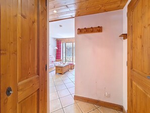 A wooden interior with a tiled floor, a sofa, a table, and a window with curtains. - Spacious apartment near slopes - 4 guests (Les Menuires)