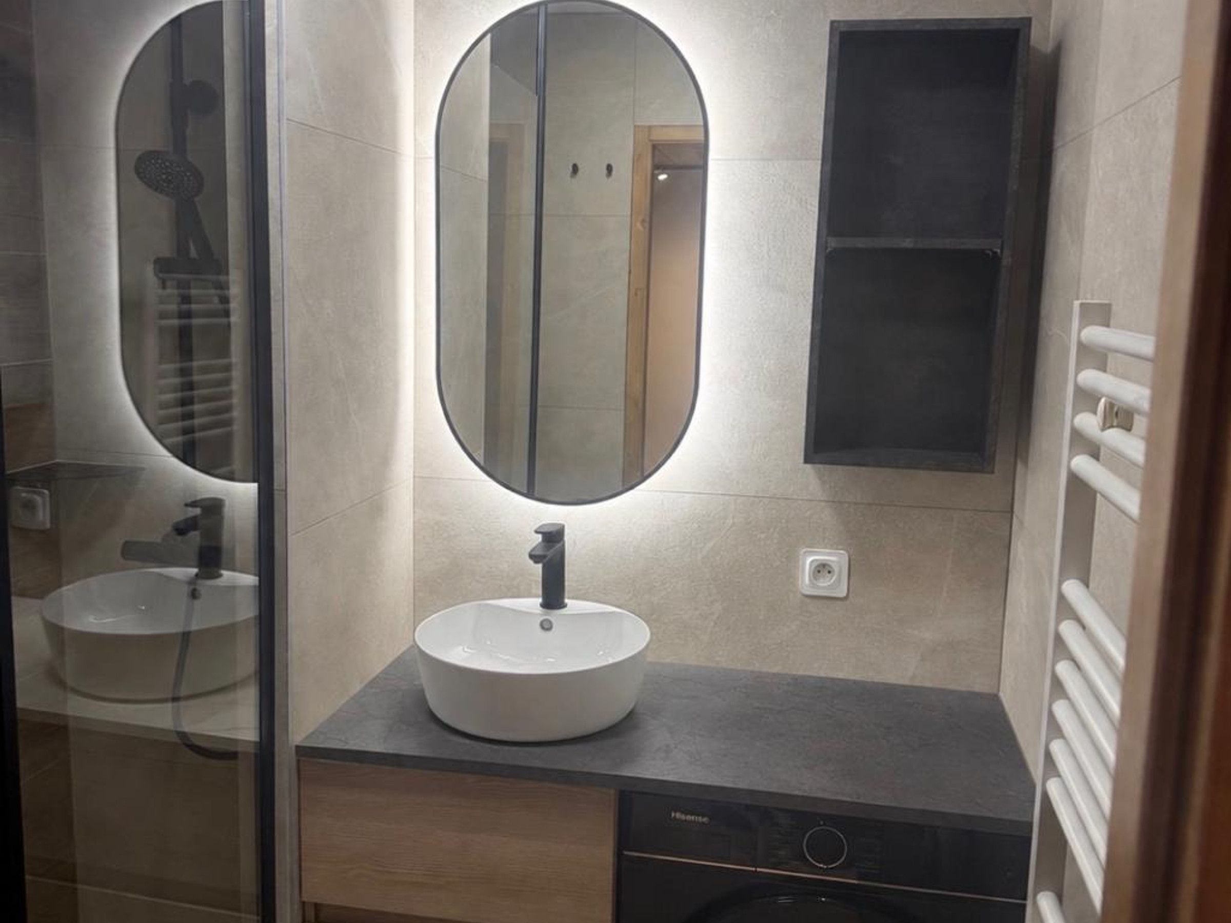A modern bathroom with a round mirror, a white sink, and a black heater.