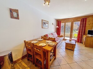 A dining area with a wooden table and chairs, a sofa, and a television on a wooden cabinet. - Spacious apartment near slopes - 4 guests (Les Menuires)