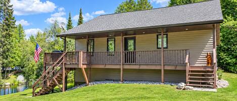 Ein zweistöckiges Lodgehaus mit einer Terrasse, einer Flagge und einem Teich im Hintergrund.