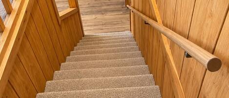A wooden staircase with a handrail, carpeted steps, and wooden walls.