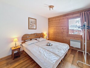 Ein Schlafzimmer mit einem hölzernen Kopfteil, einem Einzelbett, einem Nachttisch mit Lampe, einem Fenster mit Vorhängen und einer Heizung.