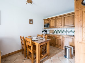 A kitchen with wooden cabinets, a tiled backsplash, and a dining table with chairs. - Spacious apartment near slopes - 4 guests (Les Menuires)