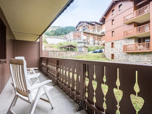 A balcony with a wooden railing, a white chair, and a view of a multi-story building with balconies. - Spacious apartment near slopes - 4 guests (Les Menuires)