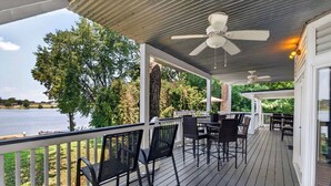 A covered outdoor deck with a view of a lake, featuring a table and chairs, and a ceiling fan. - Premium waterfront home w/ hot tub & scenic views! (Louisville)