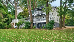 A multi-story building with a balcony, surrounded by trees and a grassy area with fallen leaves. - Premium waterfront home w/ hot tub & scenic views! (Louisville)