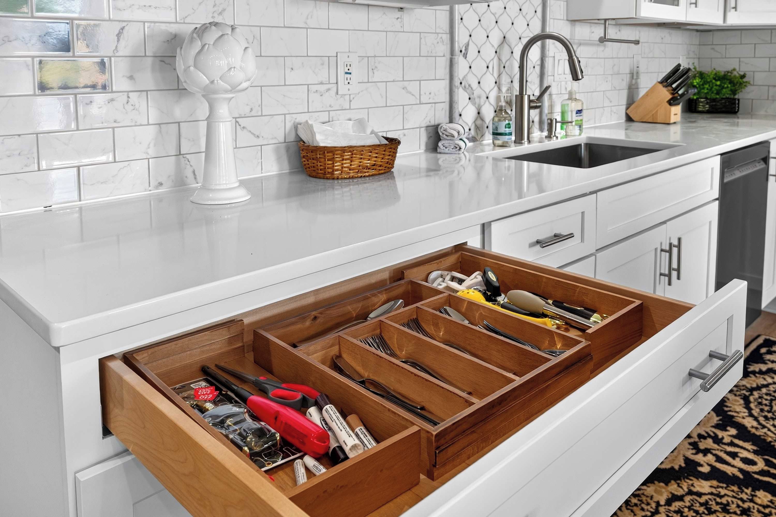 A kitchen with white cabinetry, a marble backsplash, a sink, and a drawer organizer with utensils.