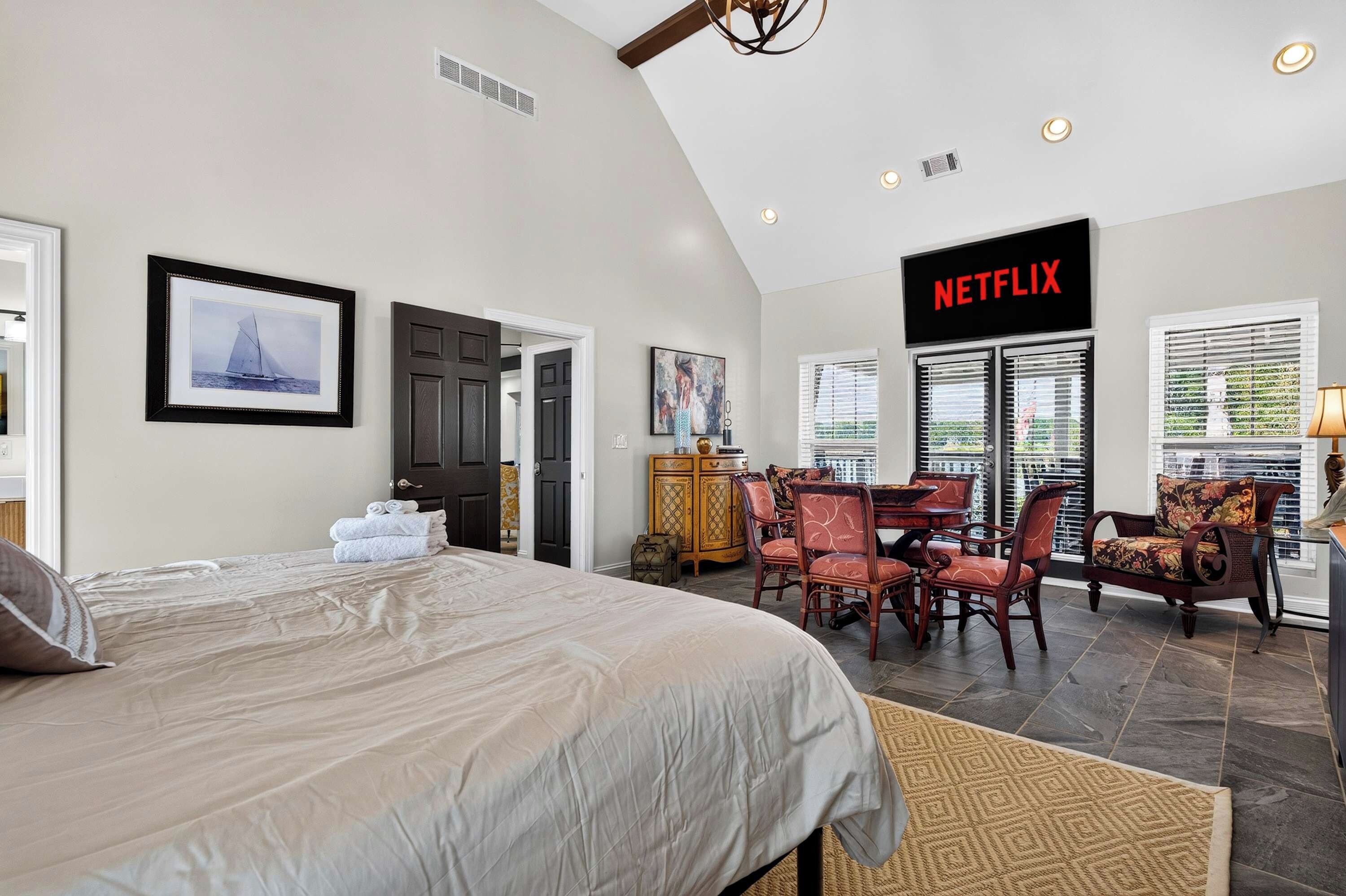 A spacious bedroom with a large bed, a dining area with chairs, a fireplace, and a sign for Netflix.