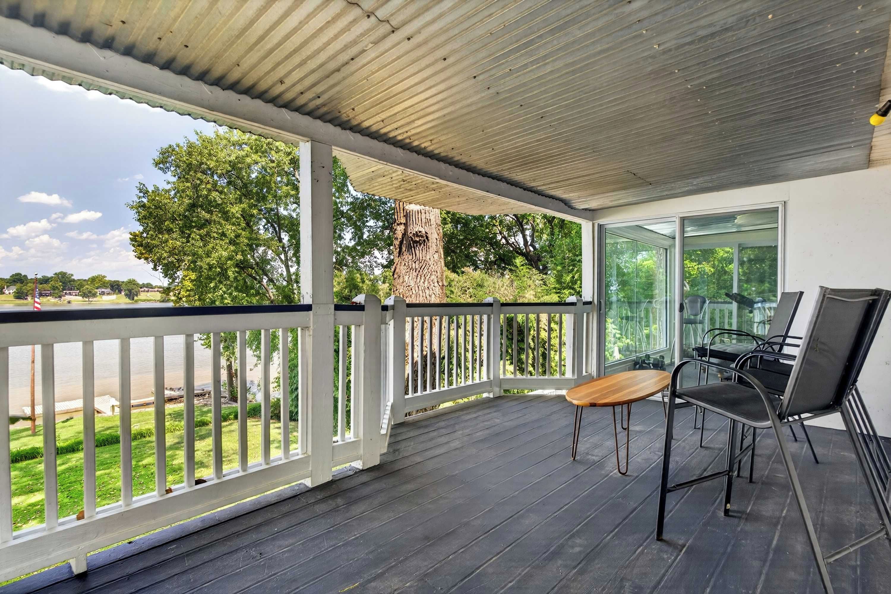 Un espace extérieur abrité, avec une table et des chaises, donnant sur un lac, et avec un arbre en arrière-plan.