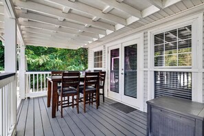 Een overdekt terras buiten met een tafel, stoelen, een barbecue en uitzicht op groen.