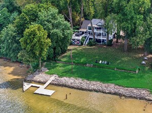 A lakeside property with a dock, a grassy lawn, and a large house with a porch.
