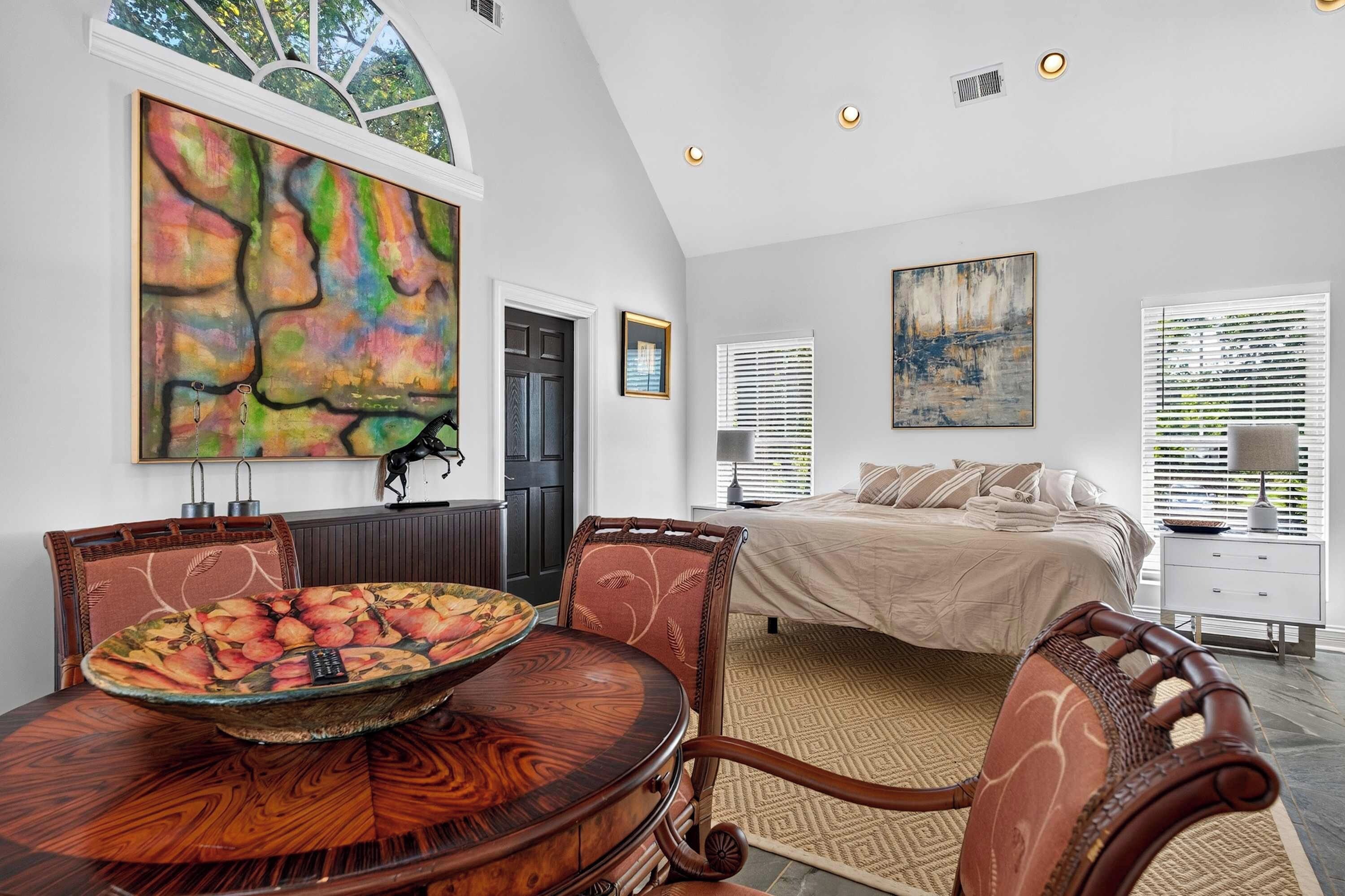 A modern bedroom with a large bed, a dining area with a round table, and two paintings on the walls.