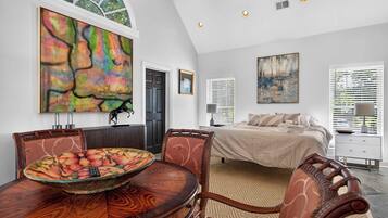 A modern bedroom with a large bed, a dining area with a round table, and two paintings on the walls.