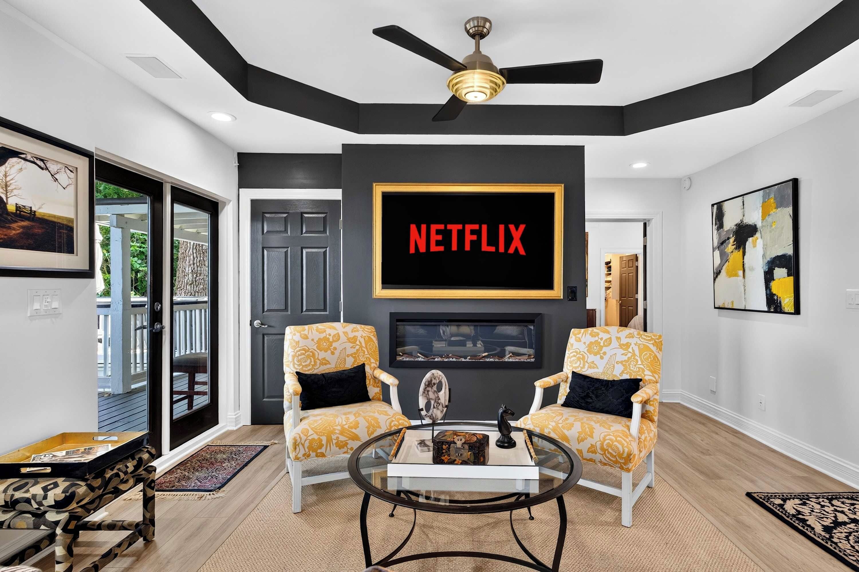 A modern living room with a large Netflix sign, two patterned armchairs, a coffee table, and a ceiling fan.