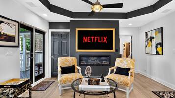 A modern living room with a large Netflix sign, two patterned armchairs, a coffee table, and a ceiling fan.