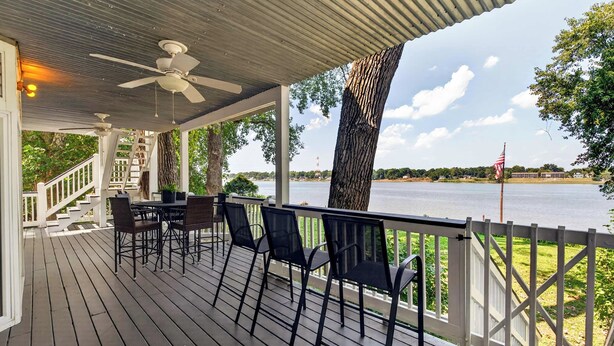 A covered outdoor deck with a table and chairs, overlooking a body of water. - Premium waterfront home w/ hot tub & scenic views! (Louisville)