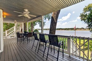 A covered outdoor deck with a table and chairs, overlooking a body of water.