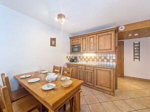 A dining area with a wooden table set for four, a kitchen with wooden cabinets, and a tiled backsplash. - Spacious apartment with balcony - 6 guests (Les Menuires)