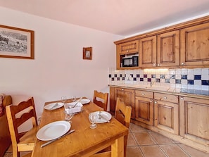 Een eethoek met een houten tafel gedekt voor twee personen, een keuken met houten kasten en een betegelde spatwand, en een inlijsting afbeelding aan de muur.