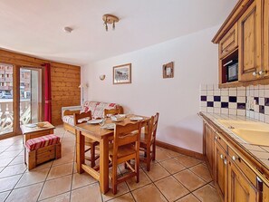 A dining area with a wooden table and chairs, a bench, and a view through a glass door. - Spacious apartment with balcony - 6 guests (Les Menuires)