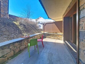 Un balcon aux murs en pierre, une table sur laquelle se trouve un plateau avec divers objets, et deux chaises.