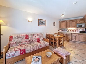 Ein gemütliches Wohnzimmer mit einer gemusterten Couch, einem Holzespeisetisch und einer Küchenzeile mit Holdekor und einer gefliesten Rückwand.