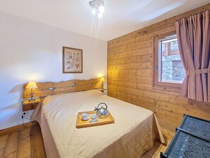 Ein Zimmer mit Holzvertäfelung, einem Bett, Nachttischlampen, einer Ablage mit Tassen und einem Teekännchen sowie einem Fenster mit Vorhängen.