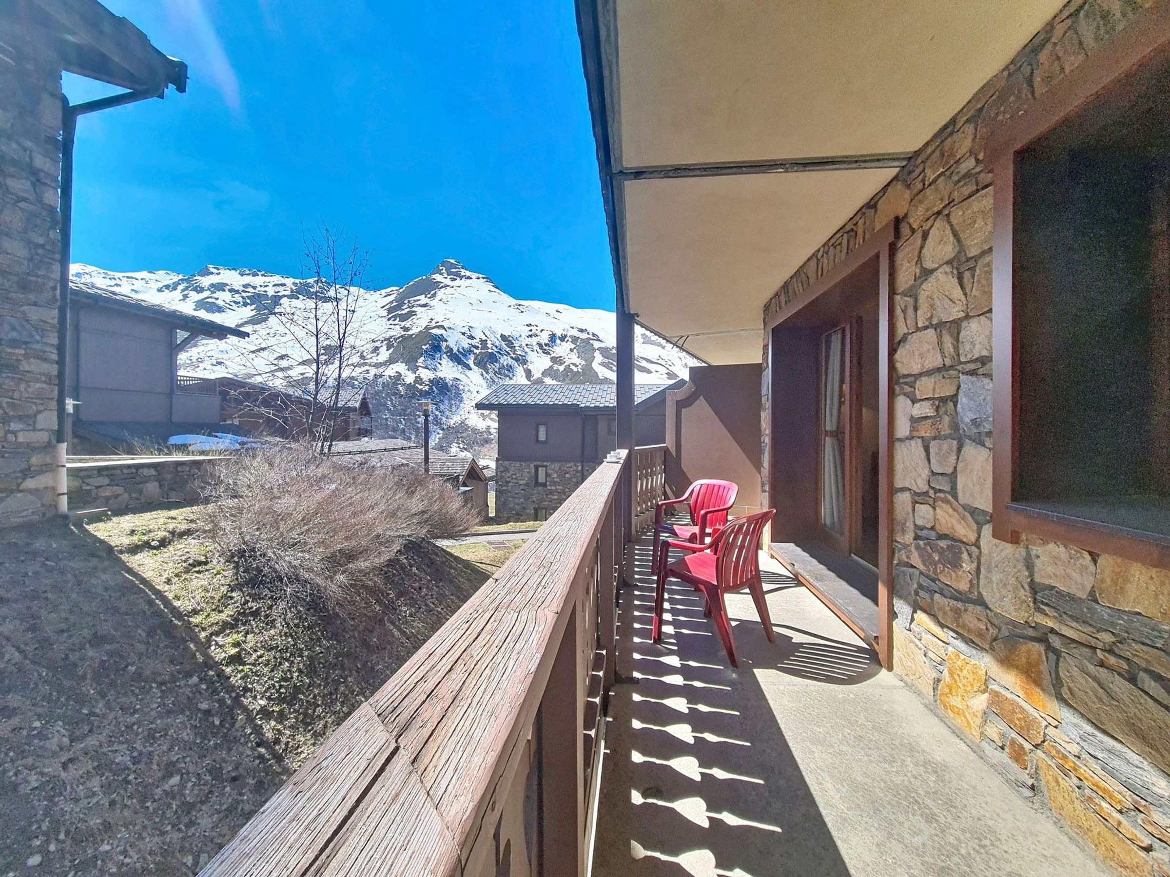 Ein Balkon mit Blick auf schneebedeckte Berge, Steinmauern und rote Stühle.