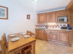 A dining area with a wooden table set for four, a tiled backsplash, and wooden cabinets. - Spacious apartment near the slopes - guests (Les Menuires)