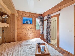 Ein Zimmer mit Holzboden, einem Bett, einem Fenster mit gemusterten Vorhängen, einem Bild an der Wand und einem Tablett mit Tassen und einem Wasserkocher.