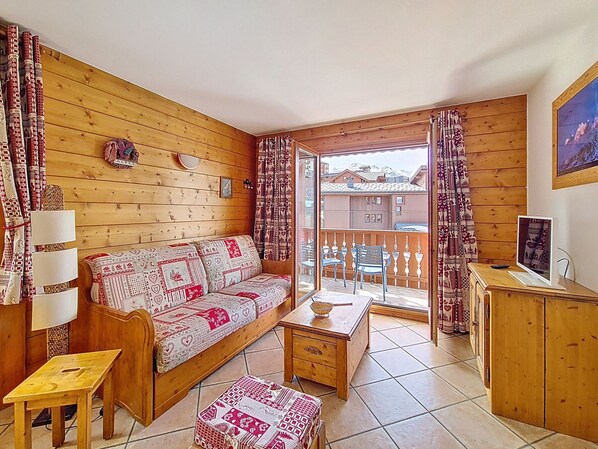 Ein gemütliches Zimmer mit einer Holzsofa, einem kleinen Tisch, einem Schrank und einem Balkon mit Blick auf Gebäude.