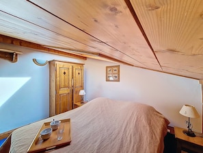 A bedroom with a bed, a wooden wardrobe, a bedside table with a lamp, and a tray with cups and a bowl. - Unique apartment near the slopes (Les Menuires)