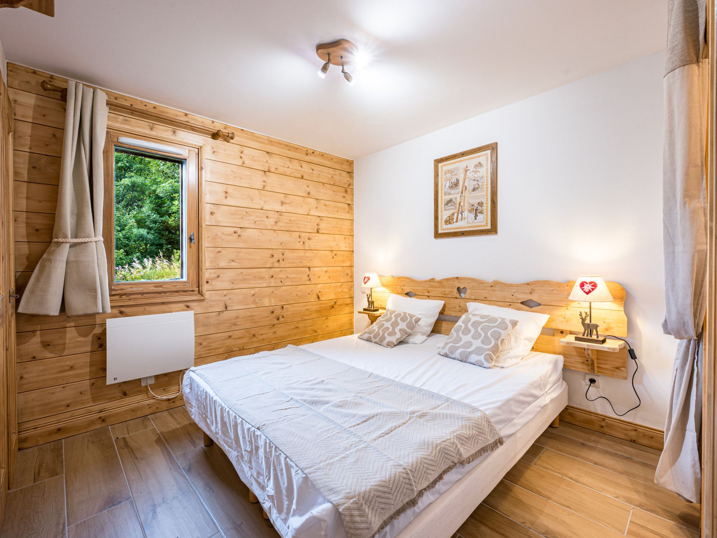 Une chambre à coucher aux murs lambrissés, avec un lit, des lampes de chevet, une fenêtre et un tableau accroché au mur.