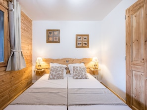 A double bed with two nightstands, each with a lamp, in a room with wooden walls and a wooden door. - Spacious apartment near slopes - 6 guests (Les Menuires)