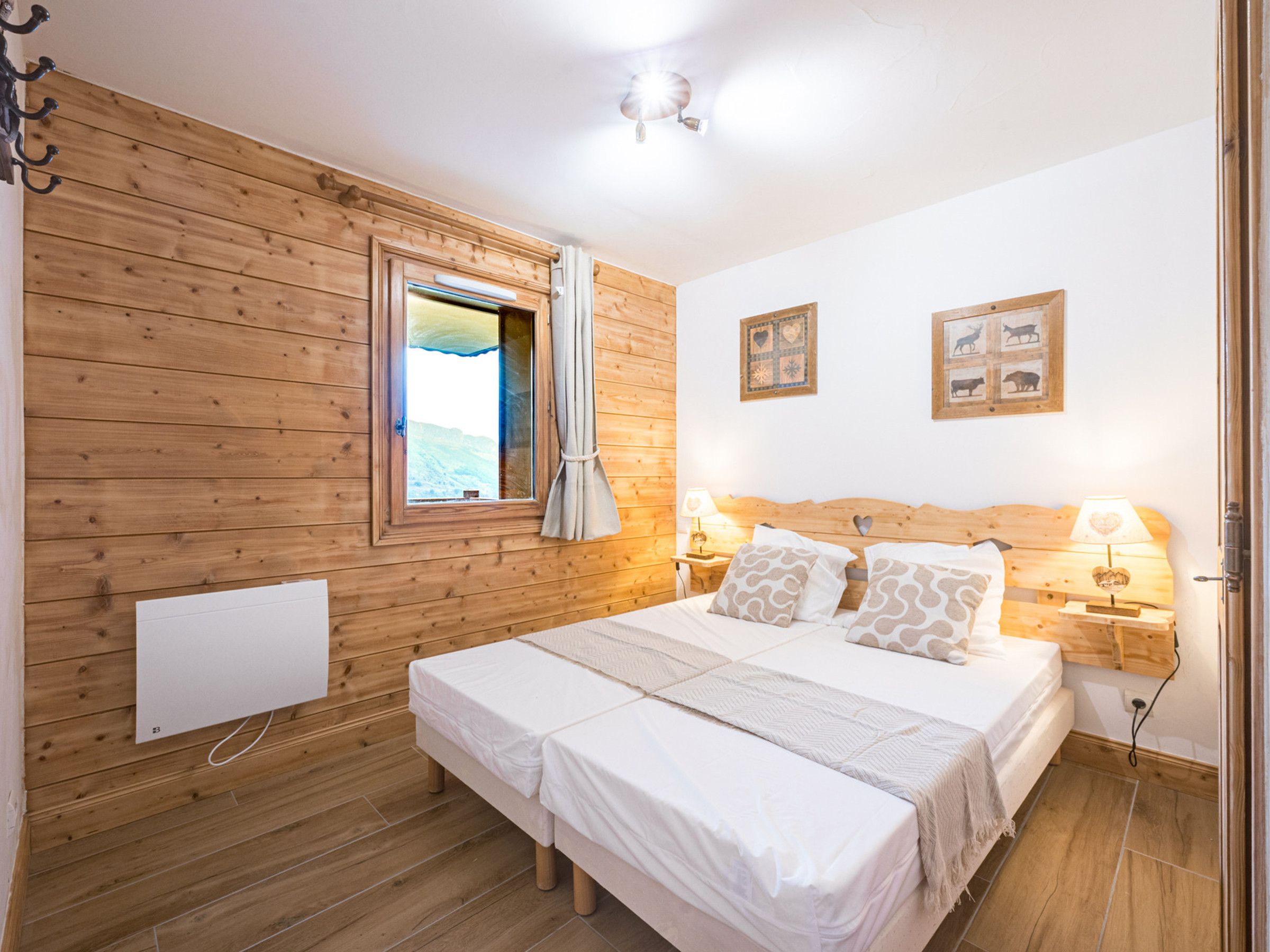 A room with a wooden wall, a bed with white bedding, two bedside tables with lamps, and a window with curtains.
