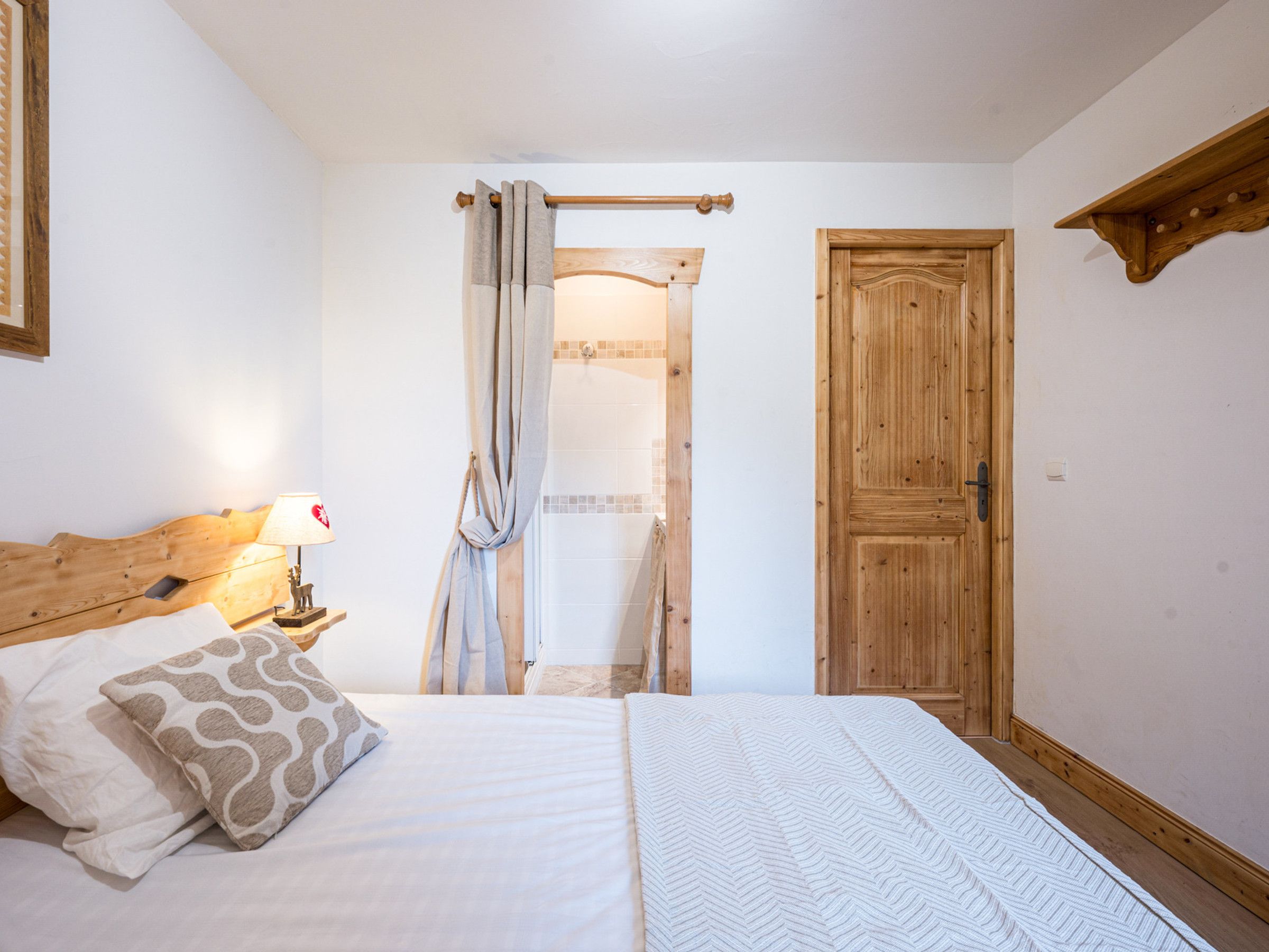 Quarto com cama, cabeceira de madeira, abajur, porta e prateleira de madeira.