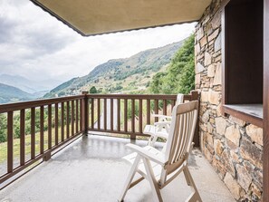 A balcony with a stone wall, a wooden railing, and two white chairs. - Spacious apartment near slopes - 6 guests (Les Menuires)