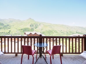 A balcony with two red chairs and a table, overlooking a mountainous landscape with buildings in the distance. - Apartment with mountain view - 3 guests (Les Menuires)
