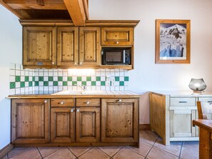 A kitchen with wooden cabinets, a tiled backsplash, a microwave, and a framed picture on the wall. - Apartment with mountain view - 3 guests (Les Menuires)