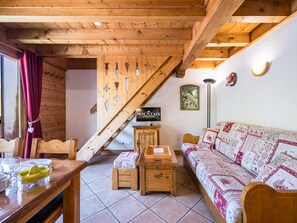 Habitació acollidora amb sostre de fusta, taula de menjador preparada amb coberts, sofà amb fons estampat i televisió sobre un suport de fusta.
