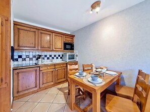 A kitchen with wooden cabinets, a tiled backsplash, a microwave, and a dining table set for two. - Spacious apartment, near slopes - 4 guests (Les Menuires)